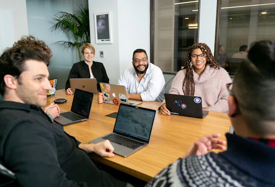 Cinco pessoas numa reunião em volta de uma mesa, cada uma com um notebook